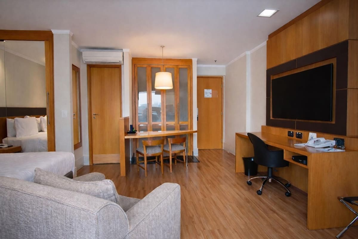 Ett hotellrum med en säng, ett skrivbord, en stol, en TV och en garderob i trä.