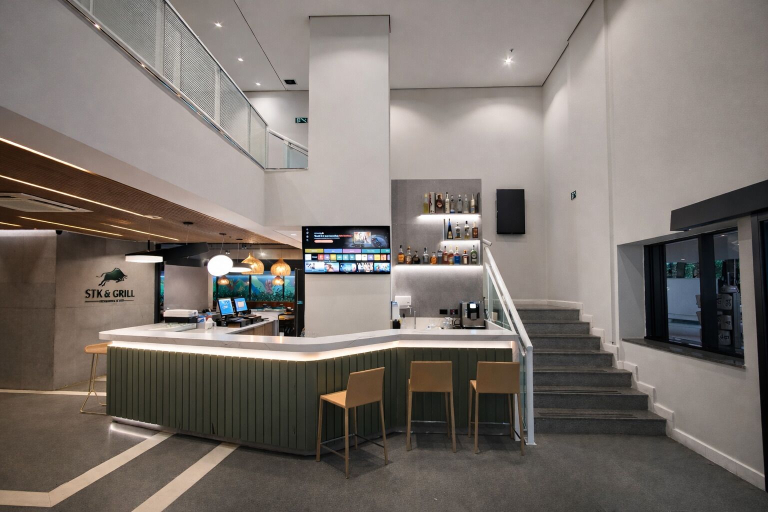 A modern bar area with a counter, seating, and a staircase leading to an upper level.