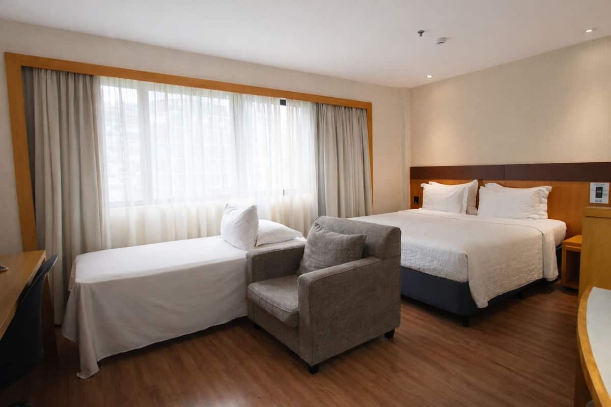 Ett hotellrum med två sängar, en stol, ett skrivbord och ett fönster med gardiner.