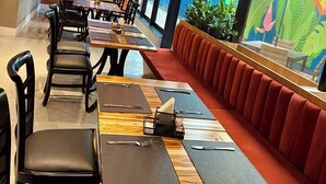 A modern restaurant interior with wooden tables, black chairs, and a red cushioned bench. - Transamerica Executive Faria Lima (São Paulo)