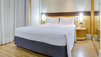 A large bed with a quilted white duvet, wooden headboard, two bedside tables with lamps, and a wooden floor.
