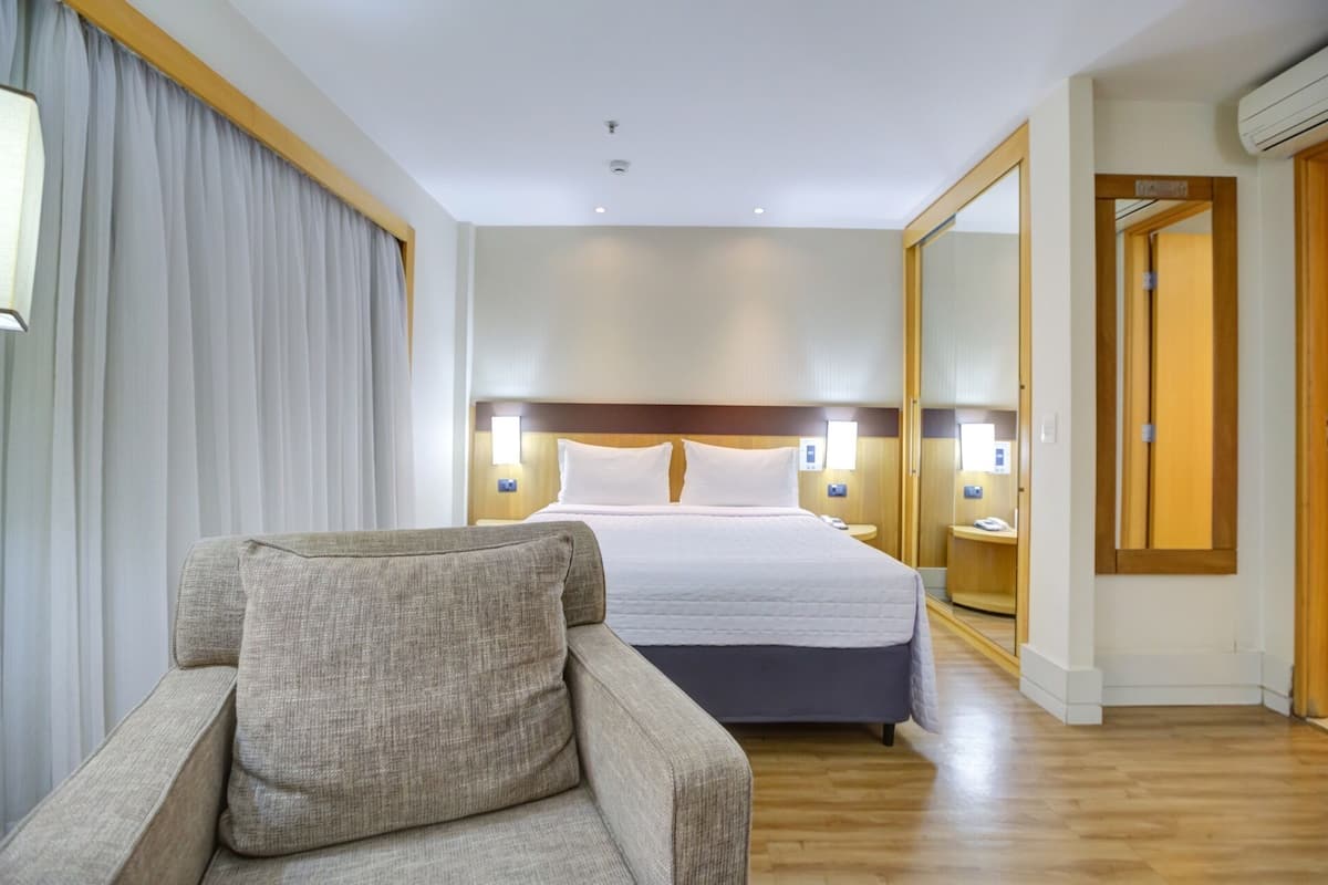 Ett hotellrum med en säng, en stol, en spegel och trägolv.