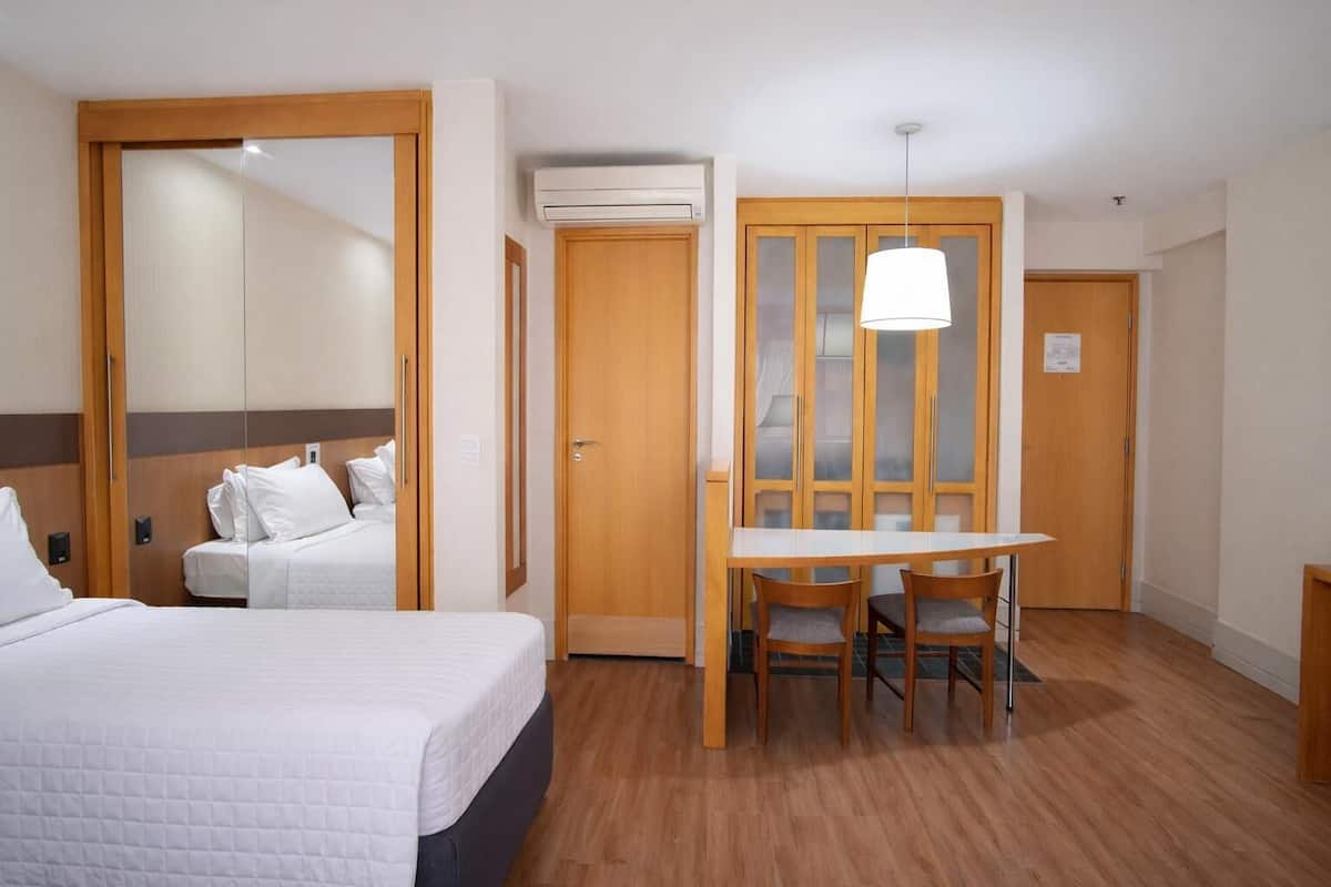 Ett hotellrum med en säng, ett skrivbord med två stolar, en garderob och en luftkonditioneringsanläggning.