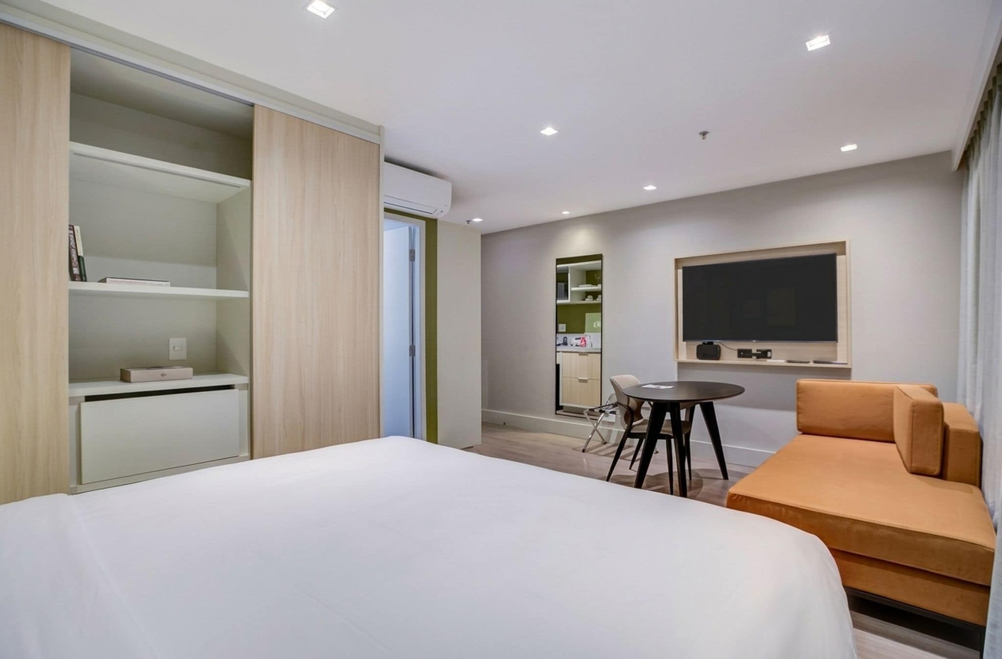 A hotel room with a bed, a desk, a chair, a sofa, and a TV.