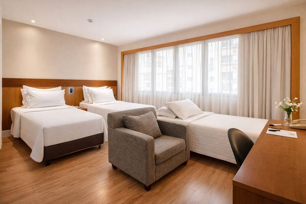 Ett hotellrum med två separata sängar, en soffa, ett skrivbord och ett stort fönster med gardiner.