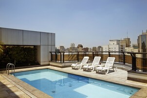 Una piscina al aire libre, sombrillas, sillones reclinables de piscina
