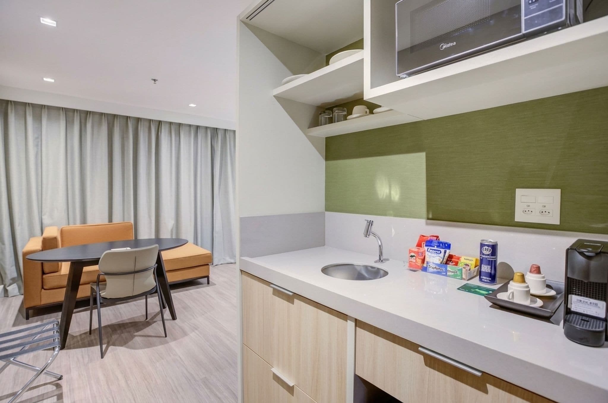 A hotel room with a dining area, kitchenette, and a large window with curtains.