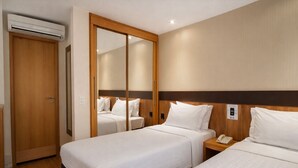 A hotel room with two beds, a wooden wardrobe, an air conditioning unit, and a bedside telephone. - Transamerica Executive Faria Lima (São Paulo)