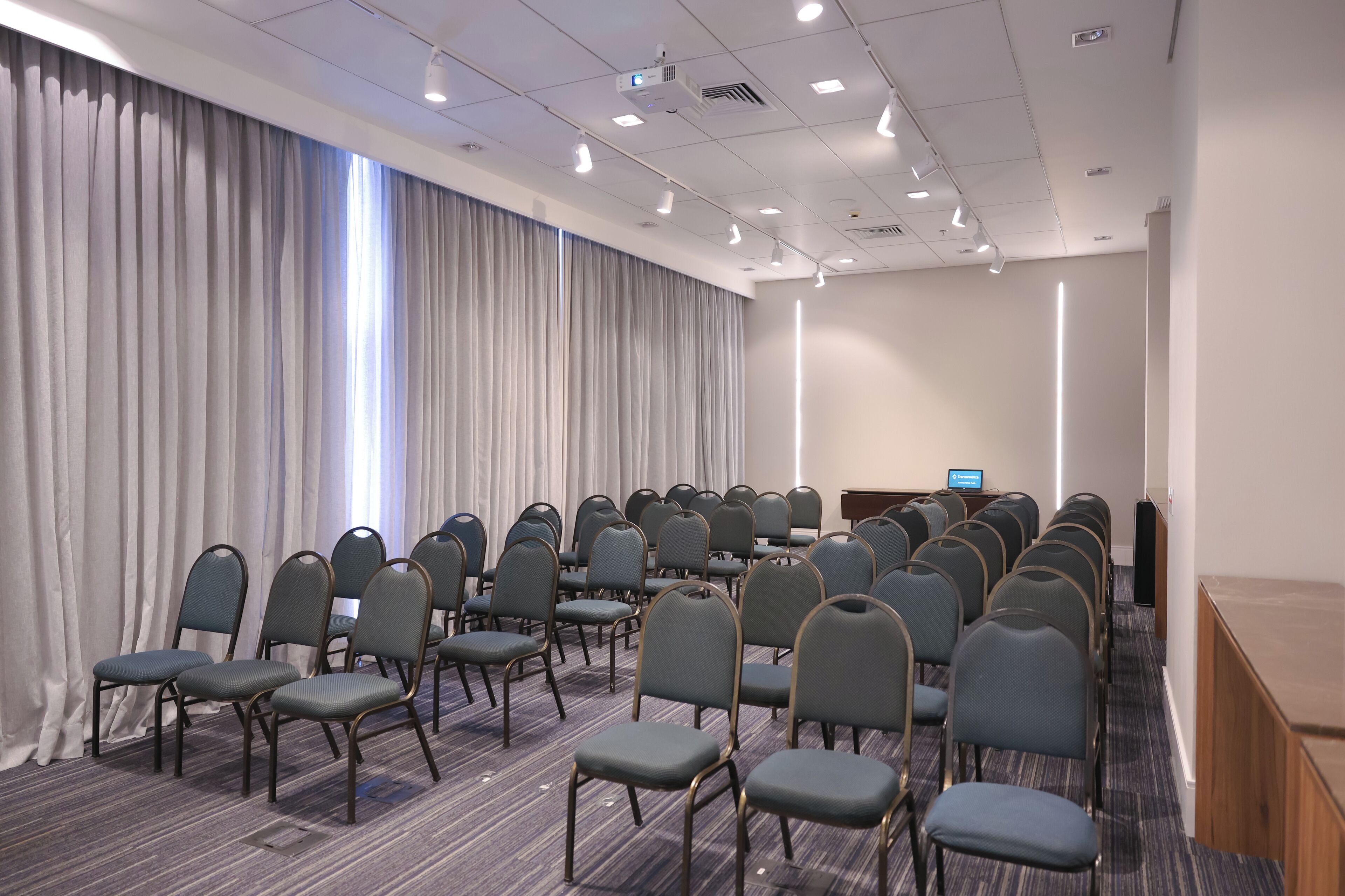 Ein Konferenzraum mit Reihen von Stühlen, einem Rednerpult und einem großen Fenster mit Vorhängen.