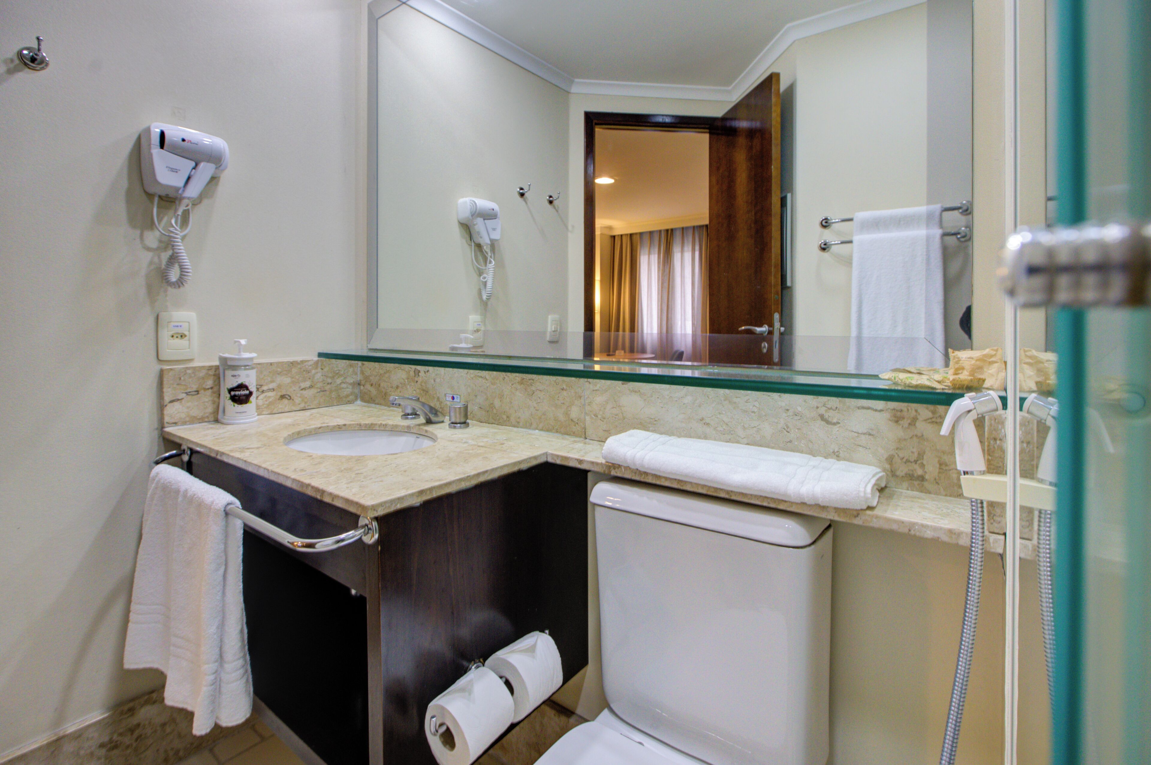 A bathroom with a marble countertop, a white sink, a mirror, a towel rack, and a shower area.