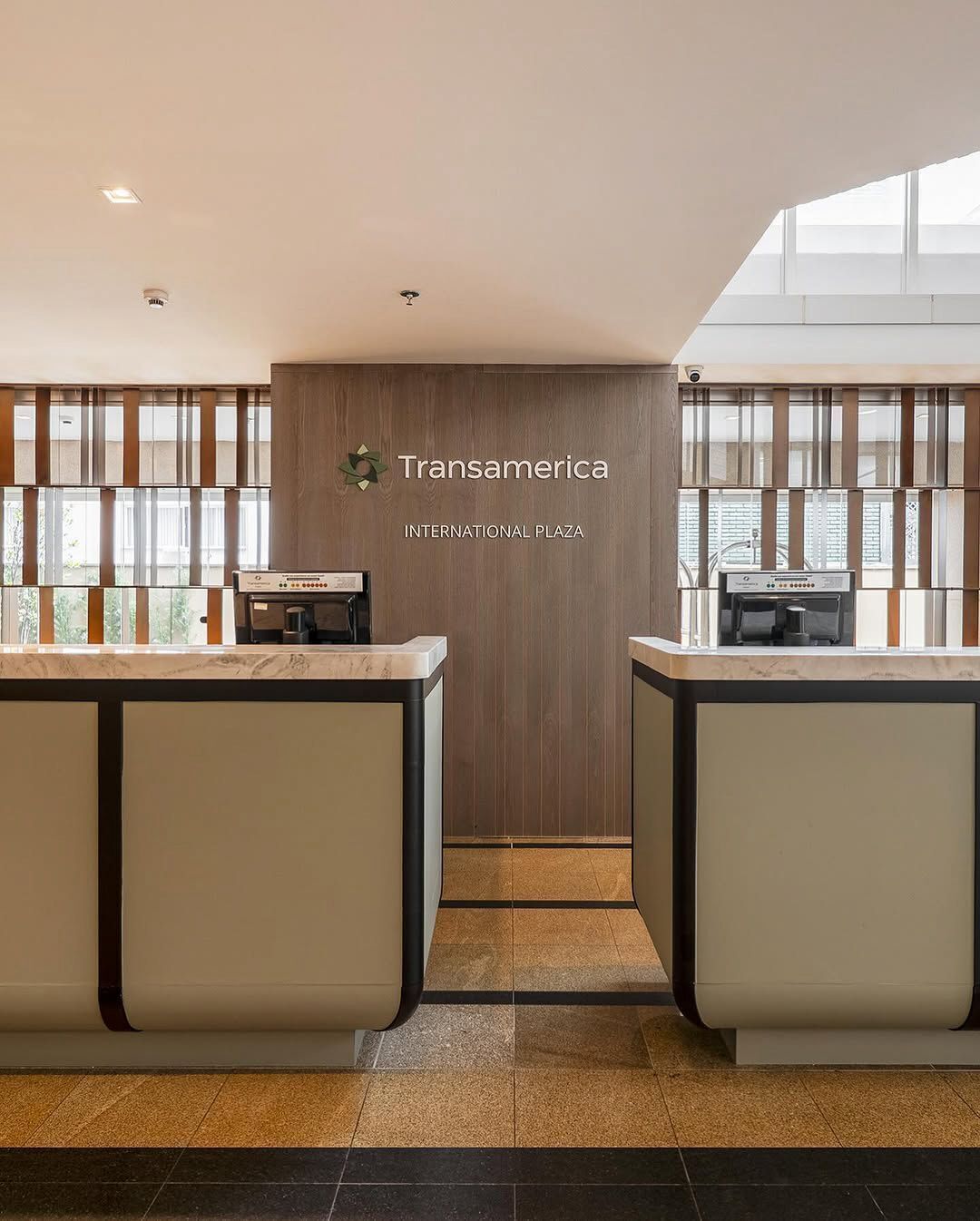 Un'area reception con due banconi, una parete in legno con il cartello 'Transamerica International Plaza' e vista all'esterno attraverso ampie finestre.