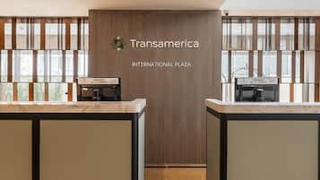 Un'area reception con due banconi, una parete in legno con il cartello 'Transamerica International Plaza' e vista all'esterno attraverso ampie finestre.