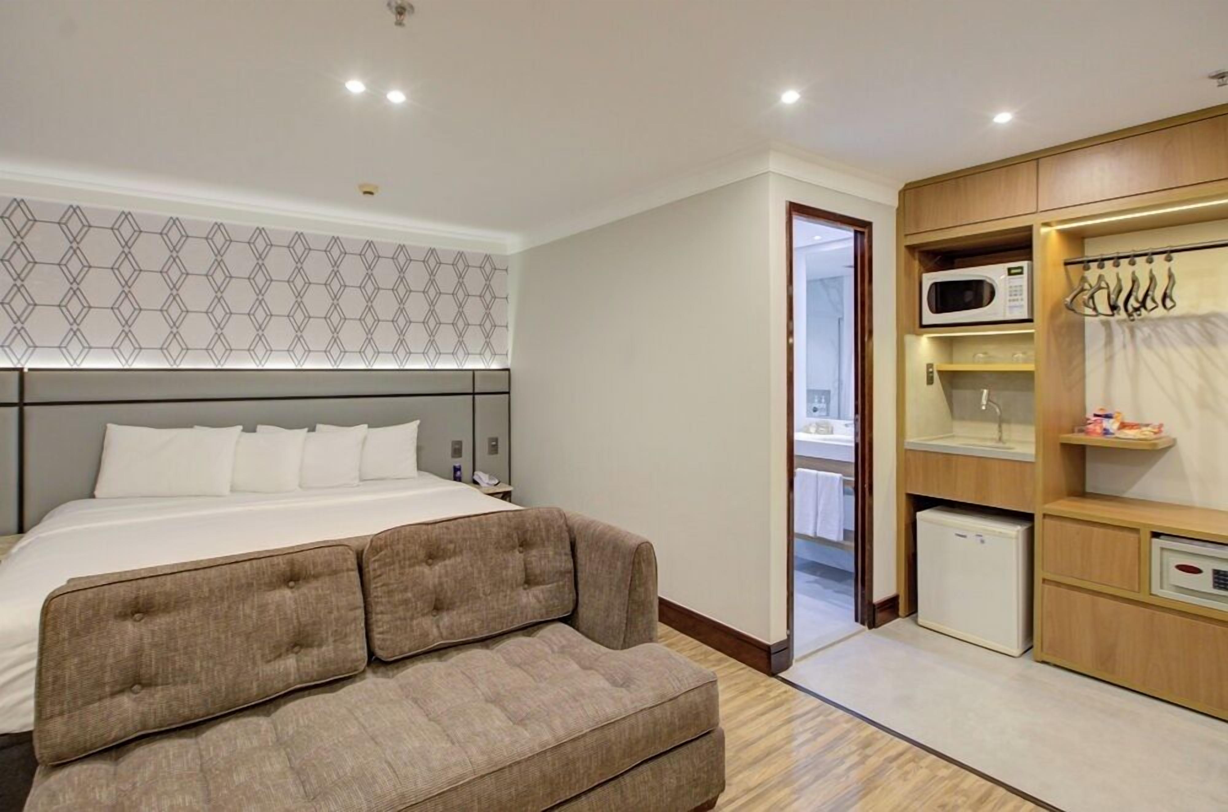 A hotel room with a bed, a sofa, a microwave, and a small refrigerator.