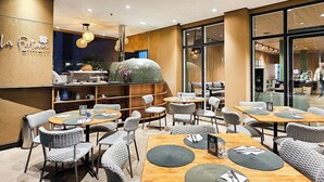 Un restaurant avec des tables rondes et des chaises en osier, un comptoir en bois et une grande fenêtre.