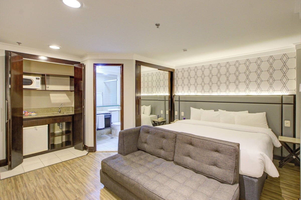 A hotel room with a bed, a sofa, a bathroom, and a kitchenette.