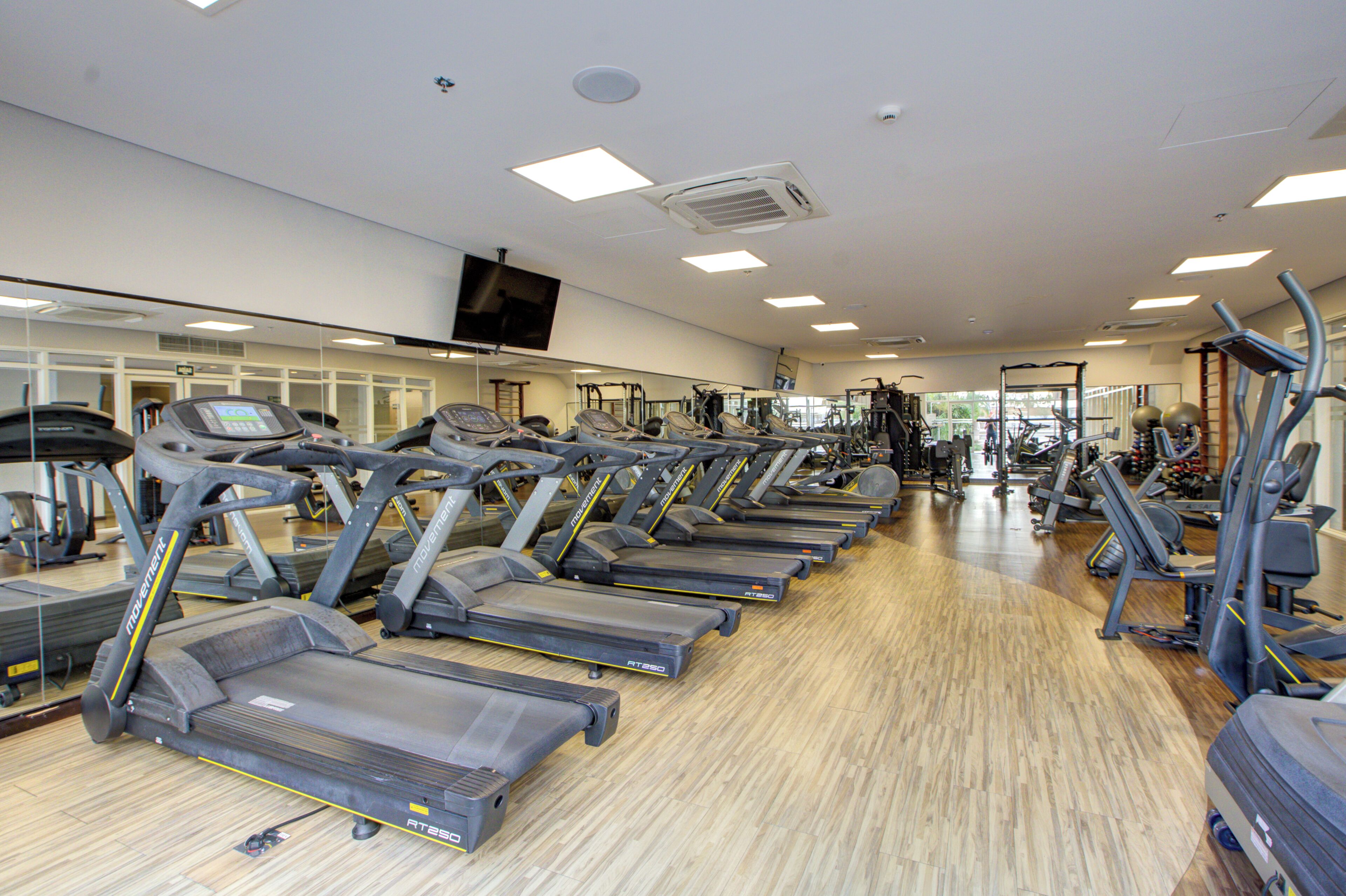 A gym with multiple treadmills, exercise equipment, and a large mirror on the wall.