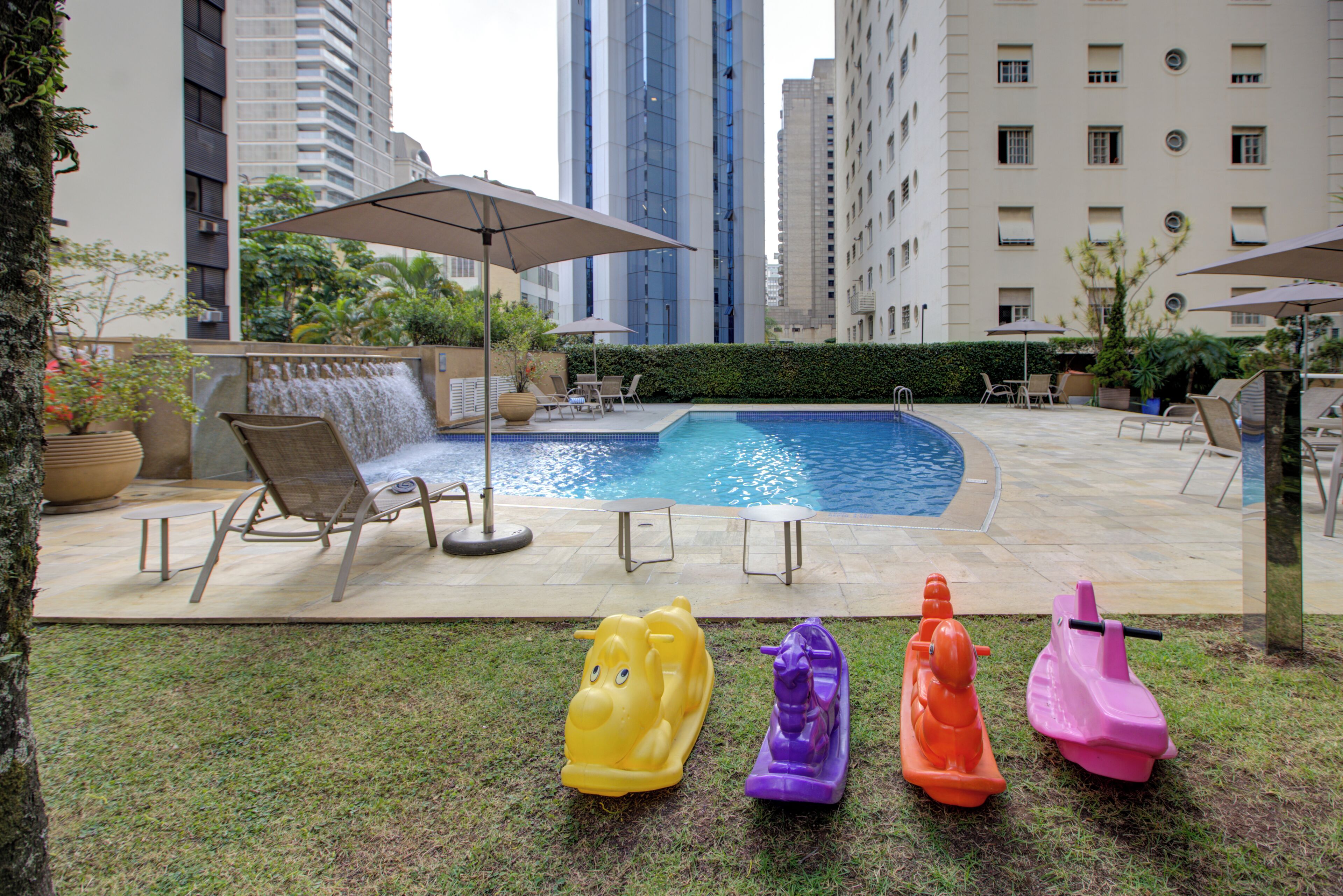 A swimming pool with lounge chairs and umbrellas, surrounded by tall buildings.