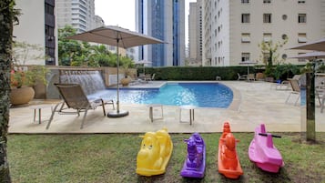 A swimming pool with lounge chairs and umbrellas, surrounded by tall buildings.