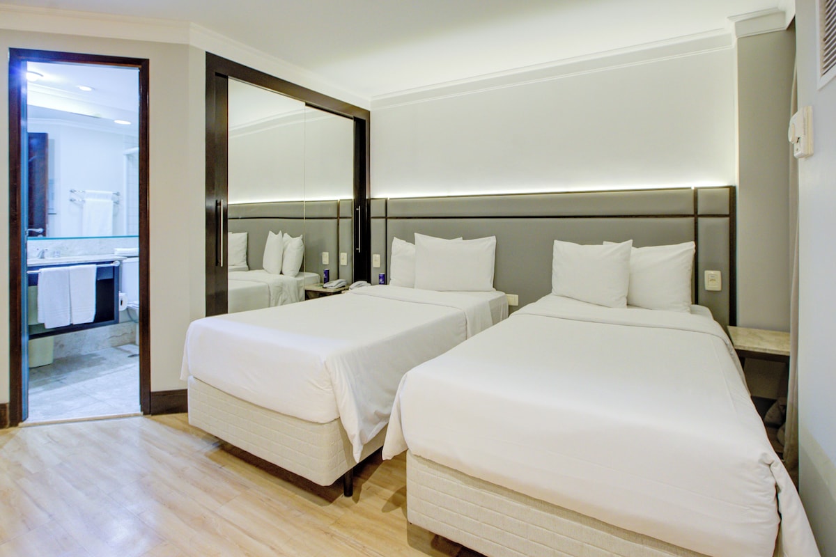 A hotel room with two beds, a bathroom, and a mirror.