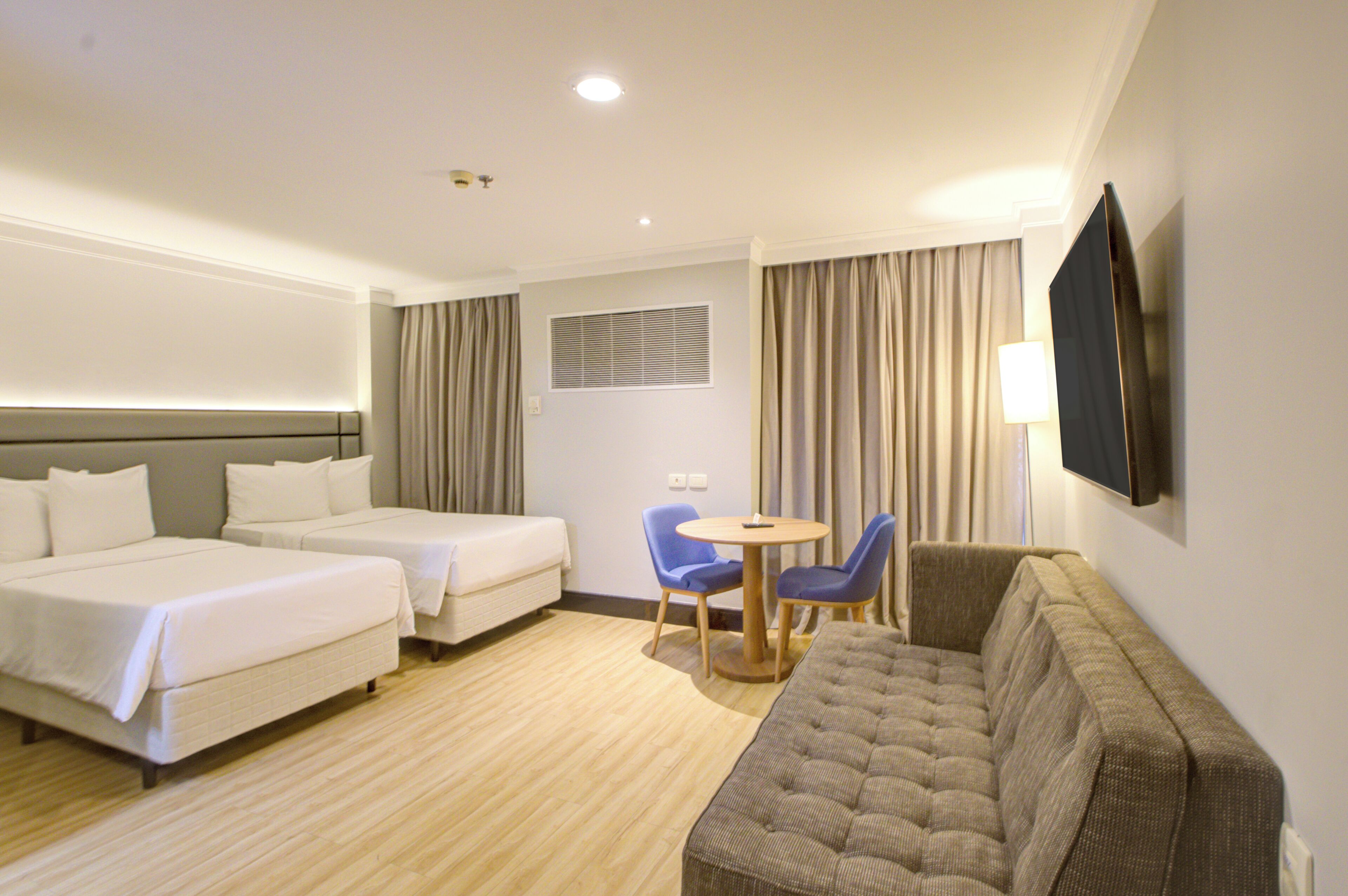 A hotel room with two beds, a sofa, a small table, and a TV mounted on the wall.