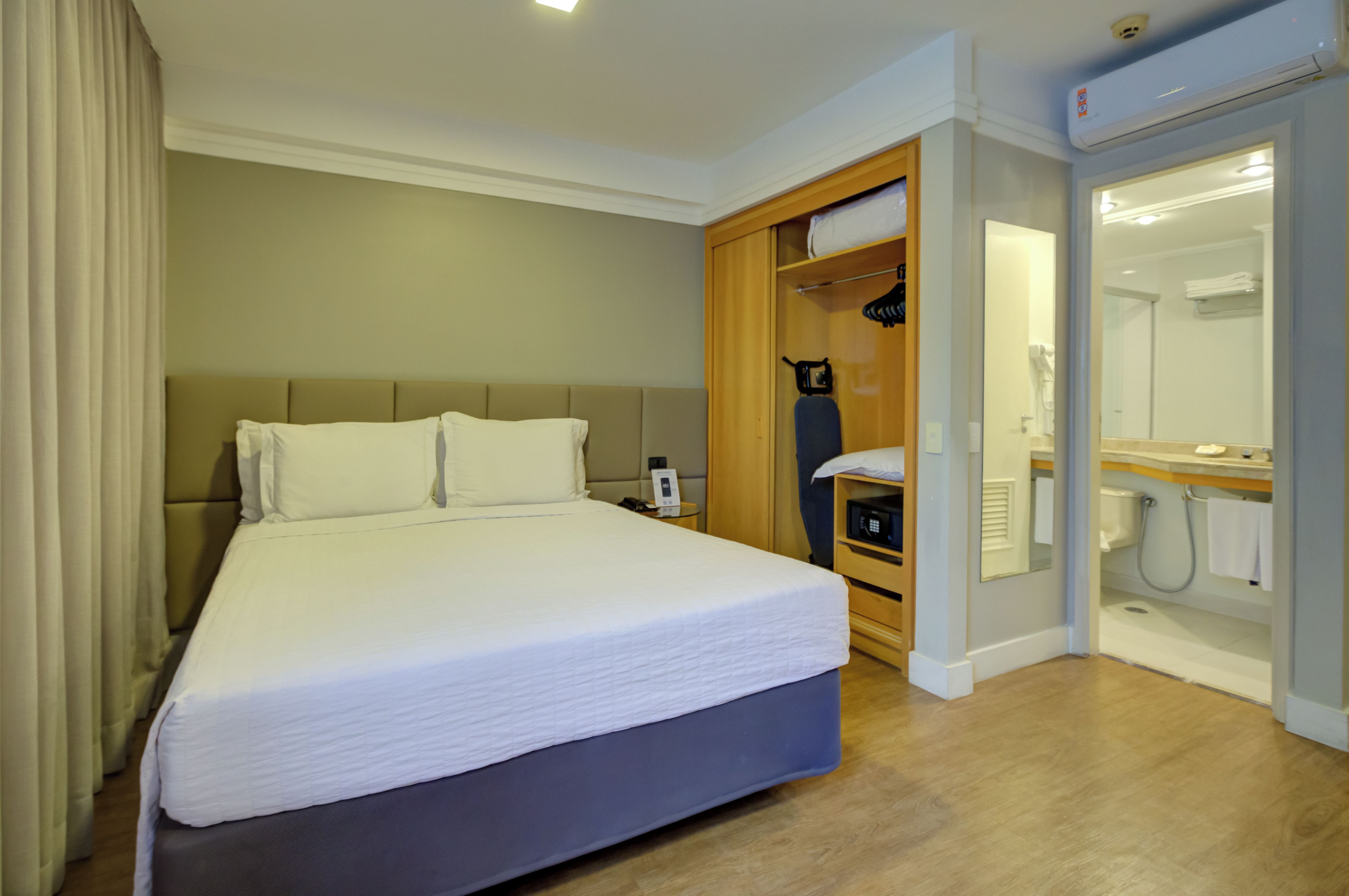 A hotel room with a large bed, a wardrobe, a bathroom with a mirror, and a shower.