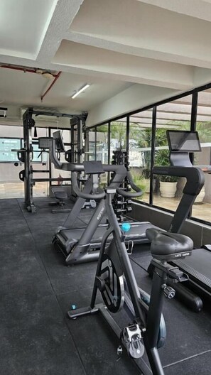 Ein Fitnessstudio mit Cardiogeräten, Krafttrainingsgeräten und einem großen Fenster mit Blick ins Freie.
