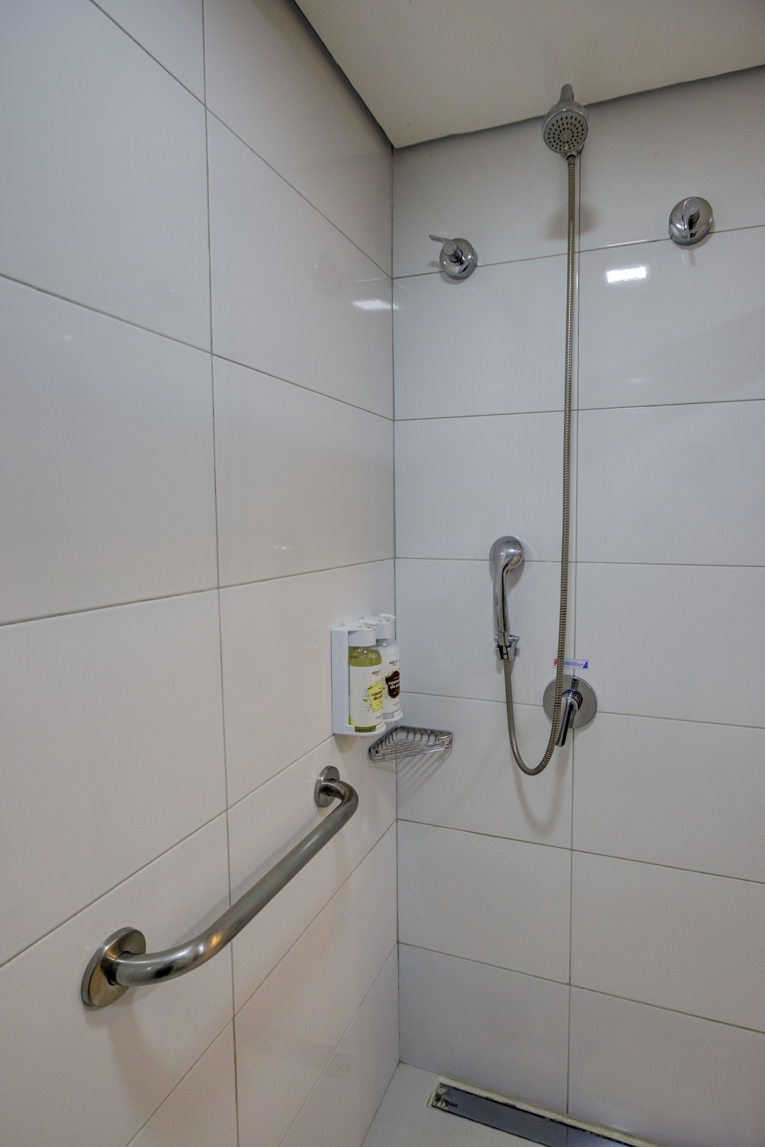 Área de chuveiro com chuveiro manual, torneira fixada na parede e outro chuveiro manual. Há um dosador de sabonete na parede.