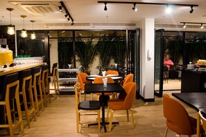 Un restaurante con varias mesas y sillas, una zona de bar y amplios ventanales.