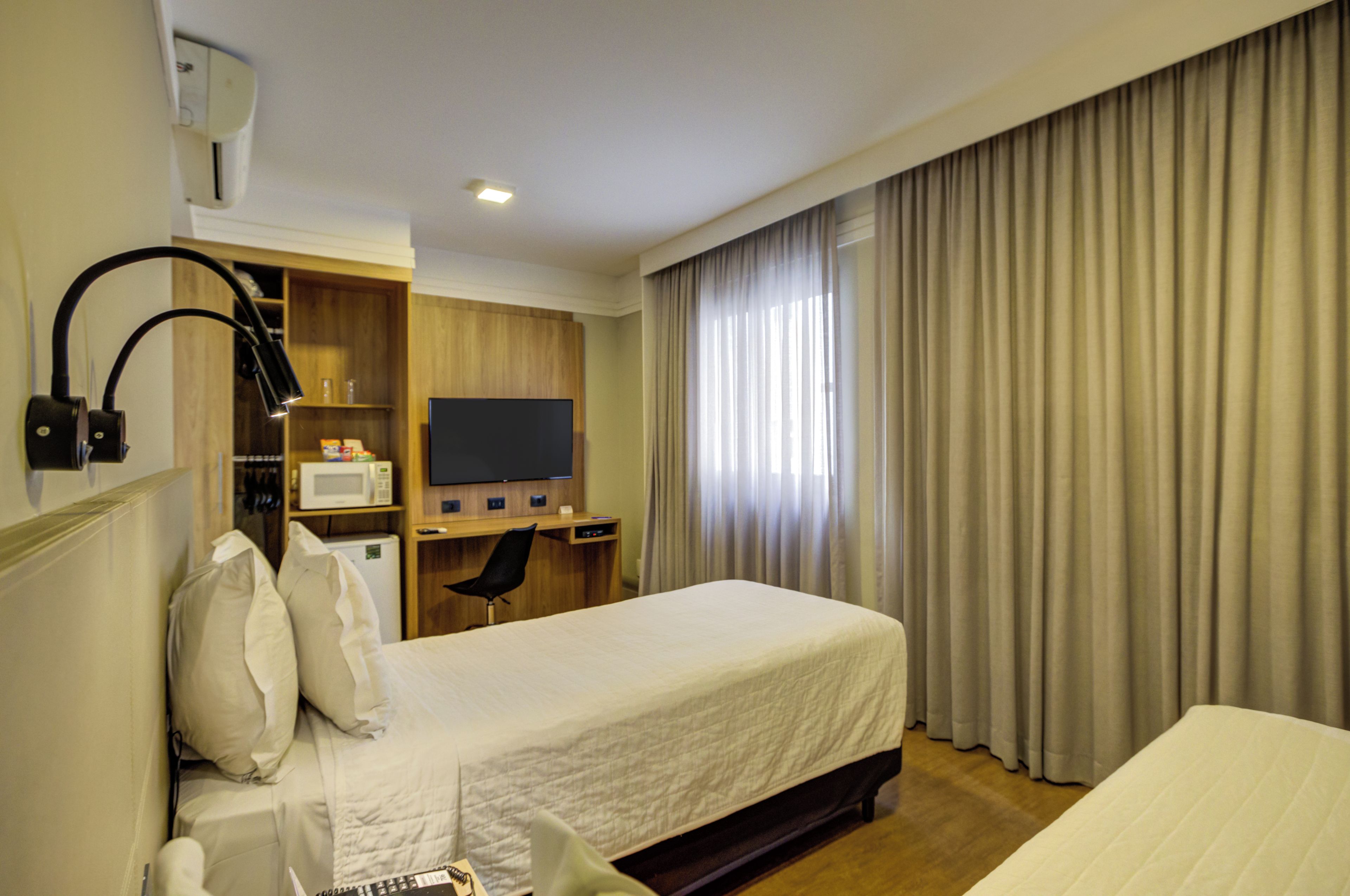A hotel room with a bed, a desk, a television, a microwave, and a window with curtains.