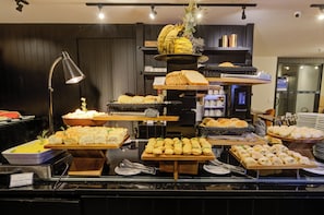 A buffet with various food items including bread, pastries, and a fruit display.