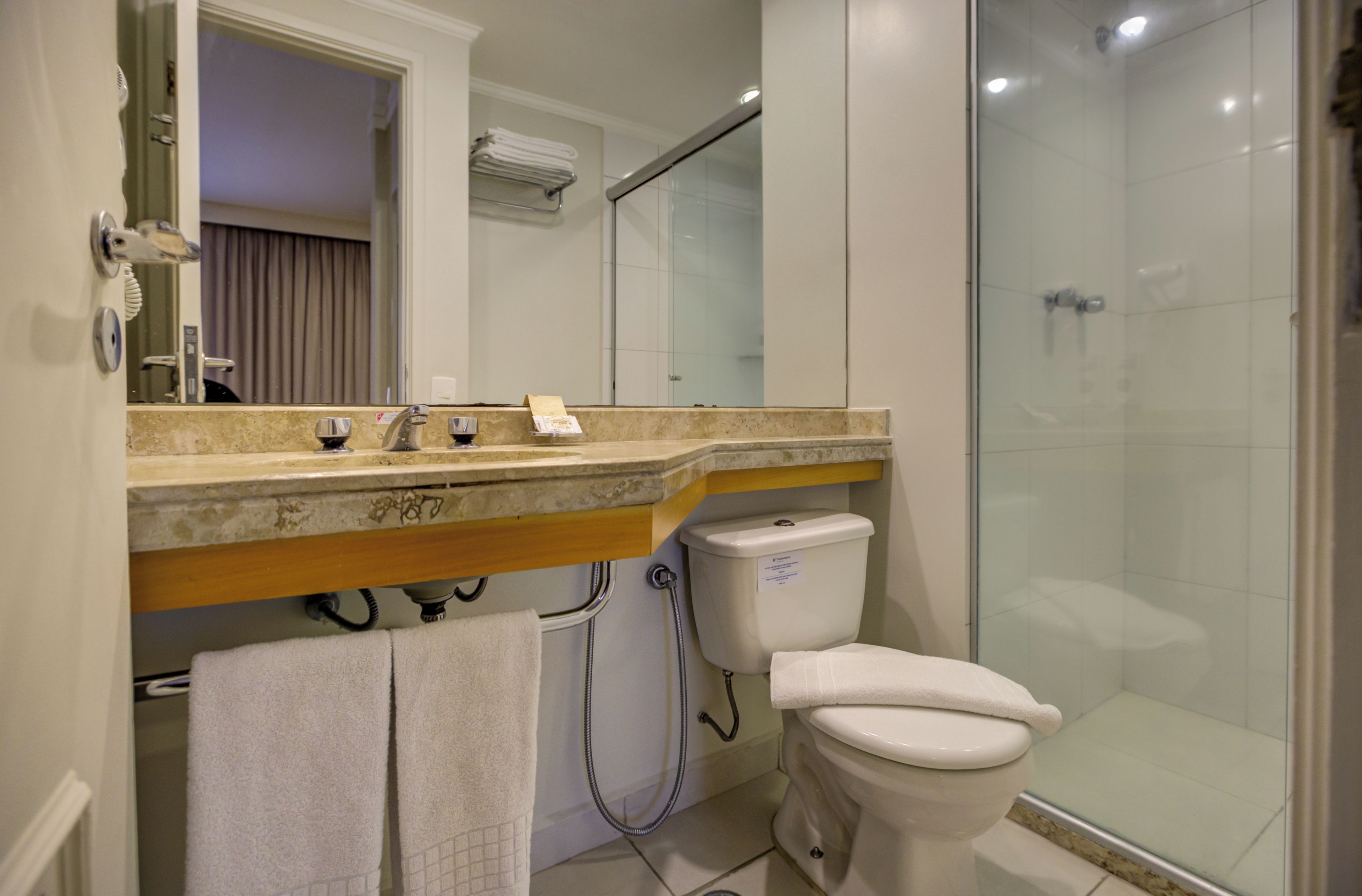Un baño con cabina de ducha de vidrio, inodoro y lavamanos con espejo.