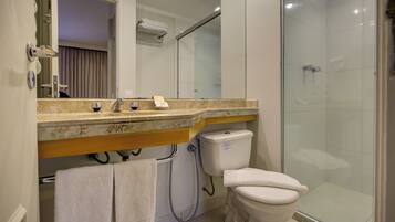 Un baño con cabina de ducha de vidrio, inodoro y lavamanos con espejo.