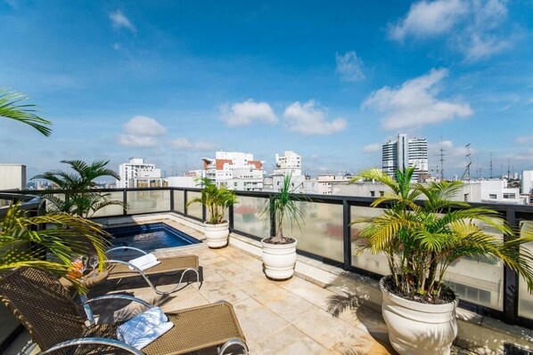 Una terraza en la azotea con piscina, sillones de descanso, plantas en macetas y vistas panorámicas de la ciudad.