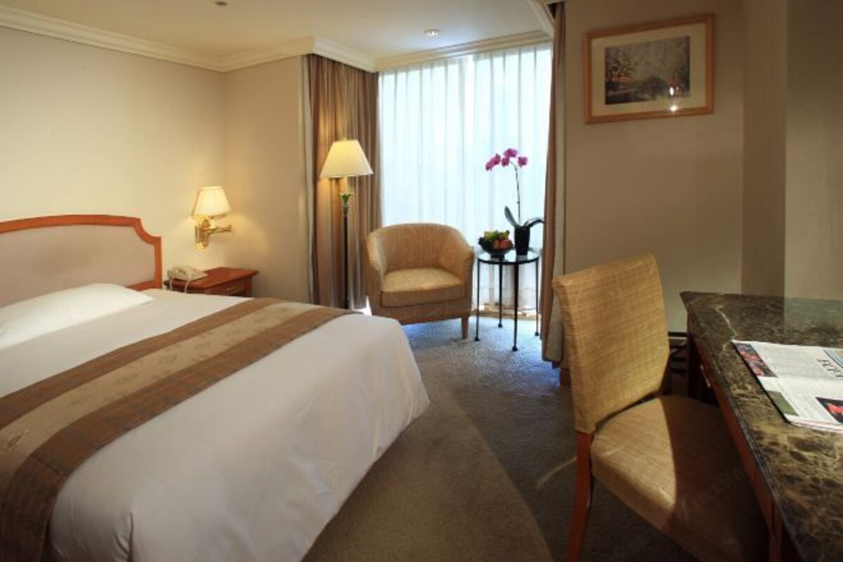 Una habitación de hotel con una cama grande, una silla, una mesita y una lámpara.