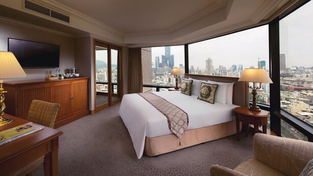 Une chambre d’hôtel avec un grand lit, une télévision, un bureau et une vue sur la ville.