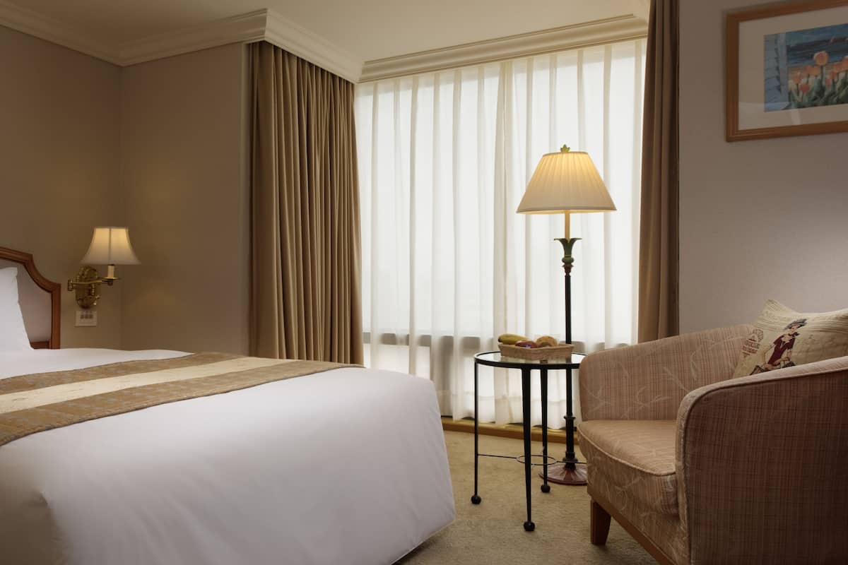Ett hotellrum med en stor säng, en stol, en lampa och ett fönster med gardiner.
