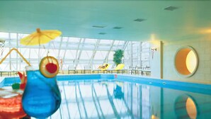 Une piscine intérieure avec des parois en verre transparent, de l’eau bleue et des chaises longues jaunes.