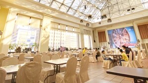 Il s’agit d’un espace intérieur vaste et lumineux, doté d’une haute verrière qui permet à la lumière naturelle d’inonder les lieux. Des tables sont disposées pour les repas, et de grandes fenêtres offrent une vue sur l’extérieur.