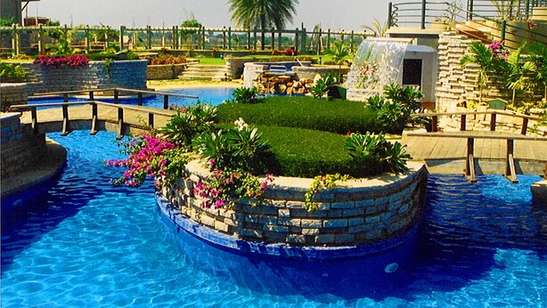 A swimming pool with a circular island, surrounded by a stone wall and featuring a small grassy area with flowers. - Angsana Oasis Spa & Resort (Bengaluru)
