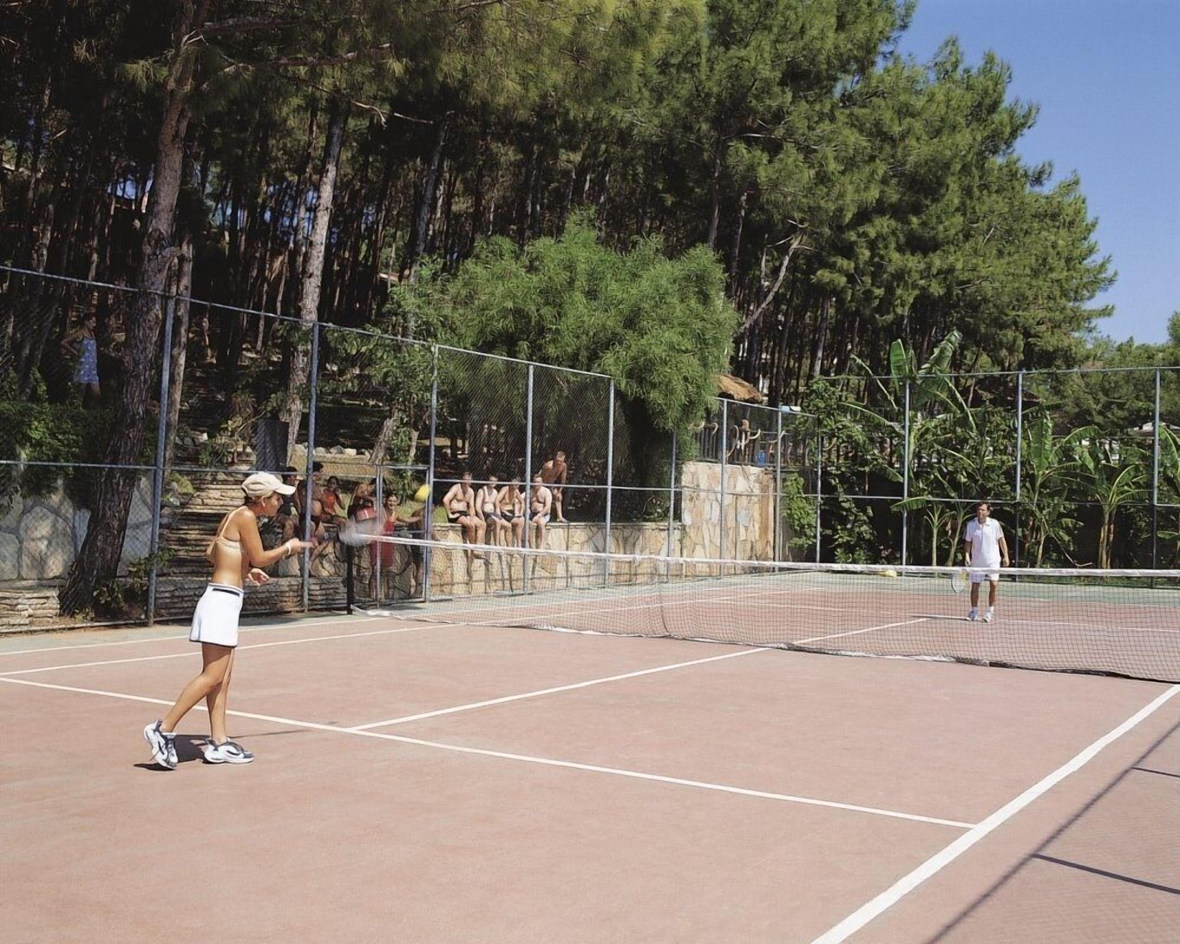 An outdoor tennis court with a net, surrounded by trees and a stone wall.