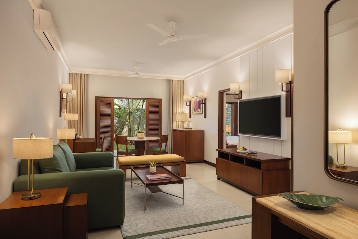A modern hotel room with a green sofa, a wooden coffee table, a flat-screen TV, and a large mirror.