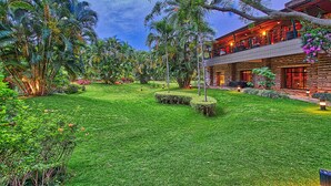 A lush, green garden with a well-maintained lawn, palm trees, and a wooden building with a balcony. - Angsana Oasis Spa & Resort (Bengaluru)