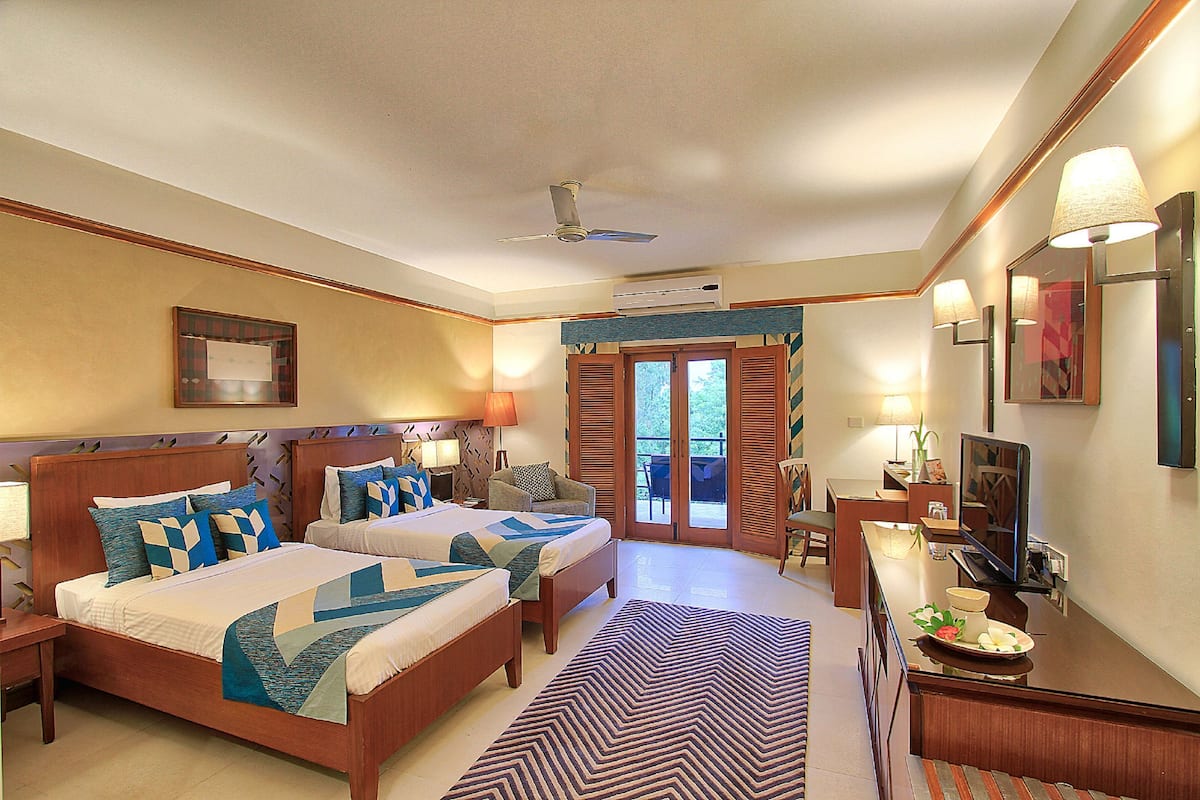 A hotel room with two beds, a TV, a desk, and a balcony.
