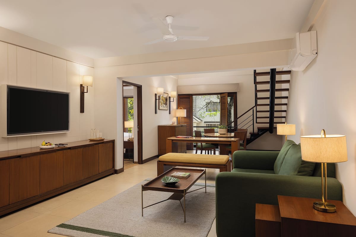 A modern living room with a flat-screen TV, a wooden coffee table, a green sofa, a lamp, and a staircase leading to an upper level.