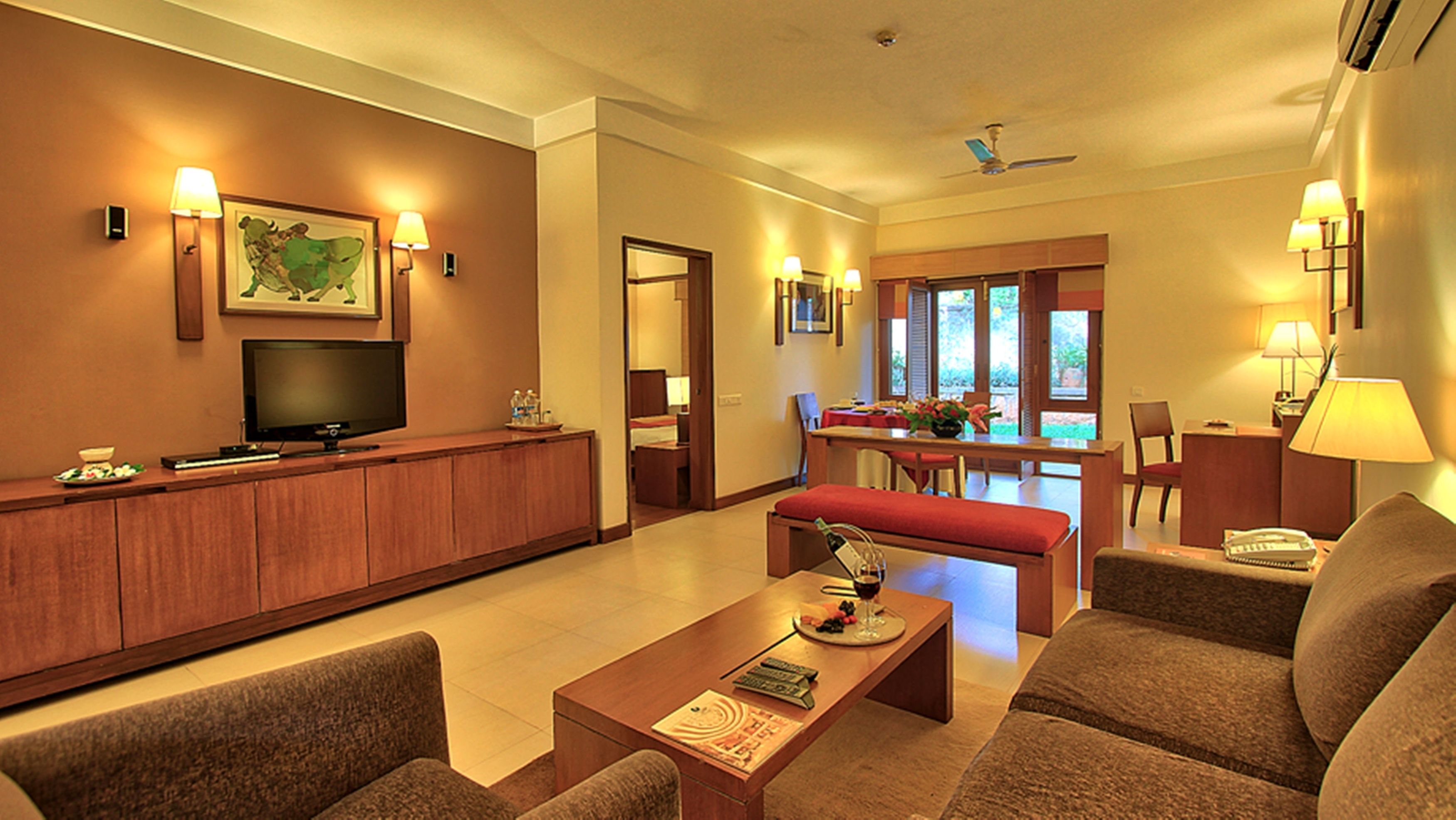 A hotel room with a TV, seating area, dining table, and a view of the outdoors.
