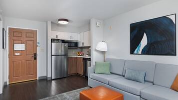 A modern apartment with a kitchenette, a grey sofa, a wooden door, and a large abstract painting.