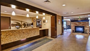 A hotel reception area with a granite counter, pendant lighting, a fireplace, and a view of the lobby. - Staybridge Suites Madison East by IHG (Madison)