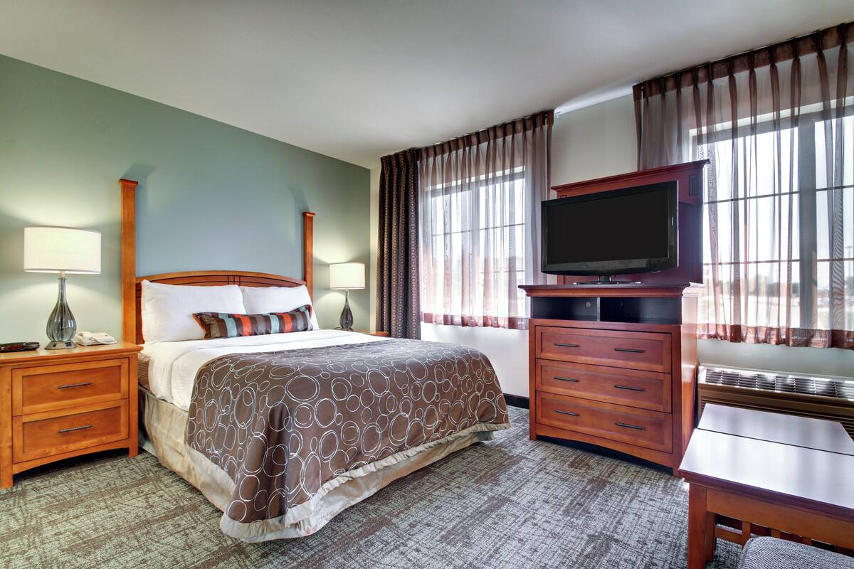 A hotel room with a bed, a TV, a desk, and a dresser.