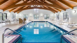 An indoor swimming pool with wooden beams, clear poolside chairs, and a tiled deck. - Staybridge Suites Madison East by IHG (Madison)