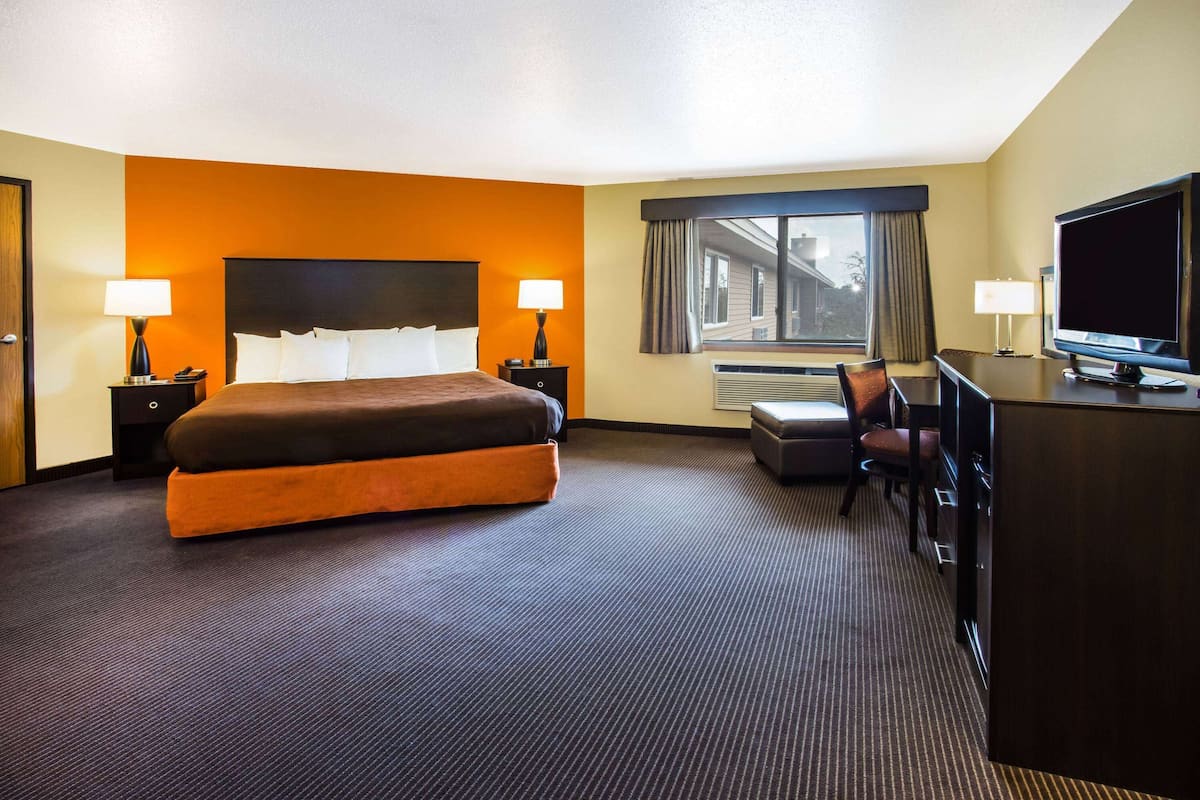 A hotel room with a large bed, two bedside tables with lamps, a desk with a television, and a window with curtains.
